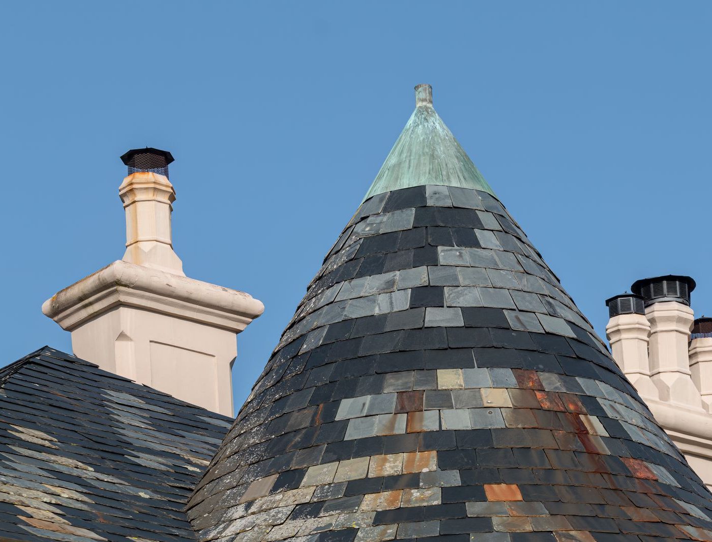 Runder Turm mit Schiefereindeckung und patinierter Kupferspitze vor blauem Himmel