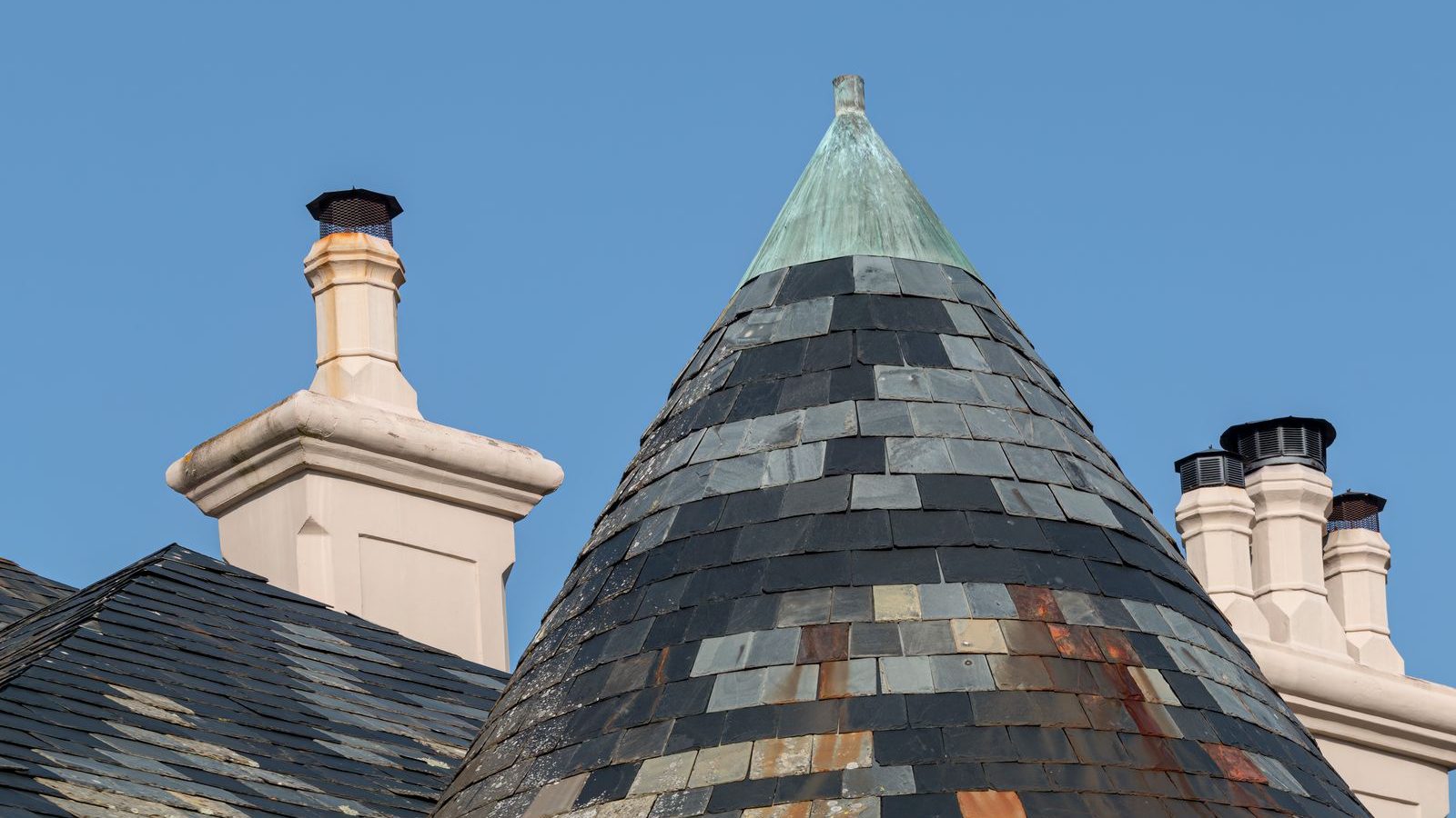 Runder Turm mit Schiefereindeckung und patinierter Kupferspitze vor blauem Himmel
